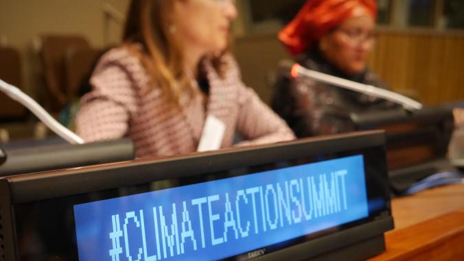 签署读取，“#climateaptionumbitumit。”智利环境部长Carolina Schmidt和U.N.副秘书长Amina J. Mohammed在背景中被夷为背景。