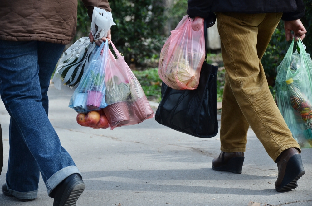 人们的脚显示行走，他们手里拿着塑料购物袋。