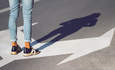 特写的人侧视图穿着黑皮鞋，蓝色牛仔裤站在街上指向不同方向的箭头标志