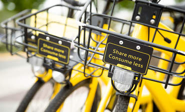 在一辆黄色的Ofo自行车上，靠近提手栏篮里“多分享，少消费”的标志，这是基于应用程序的自行车共享网络的一部分。