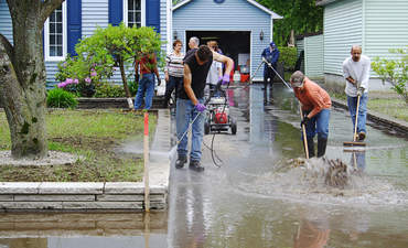 在加拿大魁北克发生灾难性洪水后，志愿者们在郊区房屋外打扫卫生