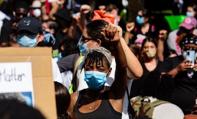 一名戴着面具的黑人领导一群示威者在佛罗里达州迈阿密市中心的一条路上游行。