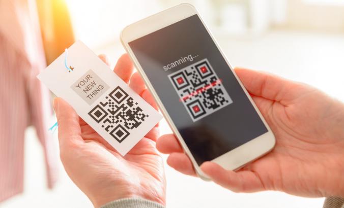 Person's hand seen holding a mobile phone and scanning QR code from a garment label in a shop