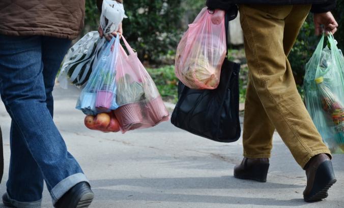 人民feet are shown walk and they have plastic shopping bags in their hands.