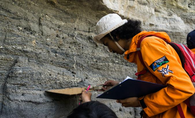 地质工程专业的学生，在砂岩和凝灰岩层上测量古水流。