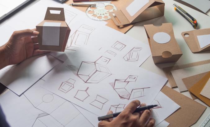 Person designing cardboard packaging and holding mockup for the design.