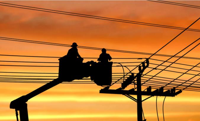 剪影:两名电工在电动缆车上工作，正在用电缆把输电线路安装到电杆上