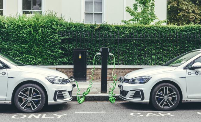 Two white Volkswagen Golf GTE cars charging at a charging point on a street in London.