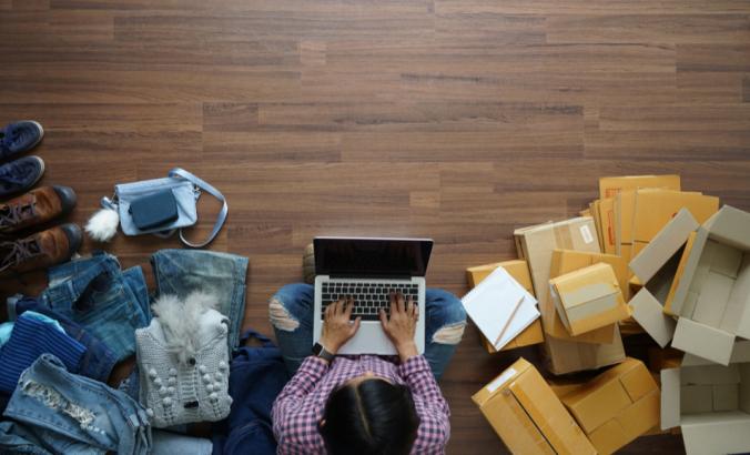 一个人在家里用笔记本电脑在木地板上工作，右边是邮包，左边是衣服和鞋子。