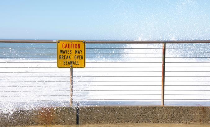 海堤上小心翼翼地标示着海浪会冲破它。水从标志上冲到人行道上。