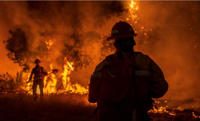 消防员（两）努力在加利福尼亚推出野火。橙色火和黑烟在背景中。