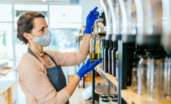 销售人员在围裙，防护面具和手套浇注玻璃银行或罐子里的油在零废物店。