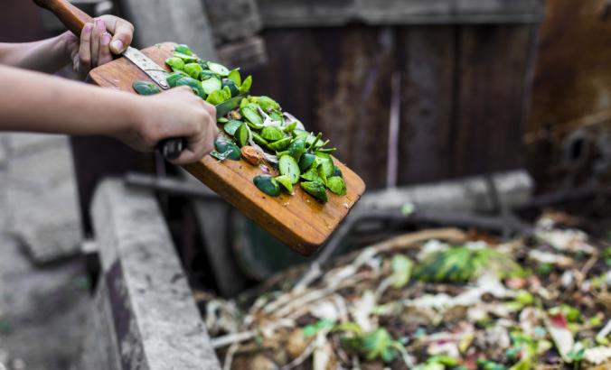 将蔬菜废物从切菜板移至花园堆肥堆的人