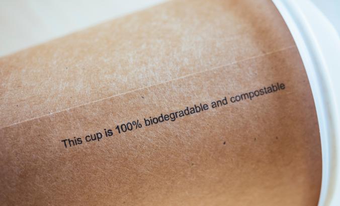 在棕色咖啡杯上，带有黑色写作，上面写着：“这个杯子是100％可生物降解且可堆肥的”