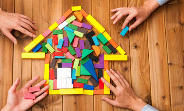 Building blocks shaped like a house, with hands on them