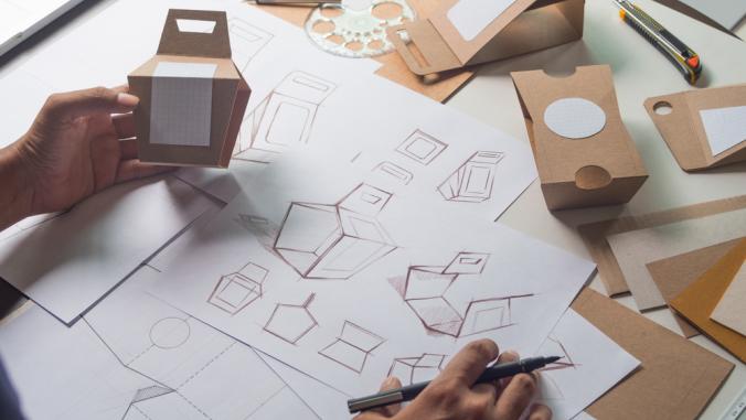 Person designing cardboard packaging and holding mockup for the design.