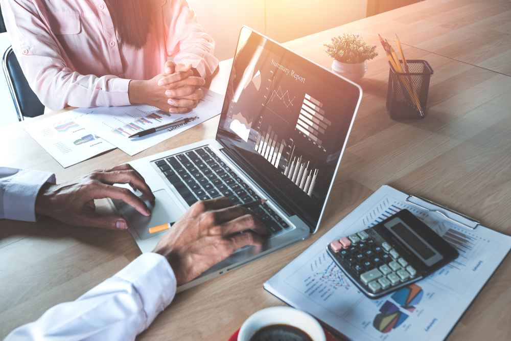 两位同事坐在桌子旁，讨论他们正在用笔记本电脑浏览的数据。