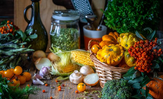 Autumn vegetables on a wooden table: pumpkin, orange pepper, paprika, mushrooms, corn, sweet potato yam, squash, cauliflower, broccoli tomatoes herbs basil
