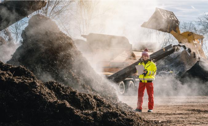 Worker standing with clipboard in industrial compost plant